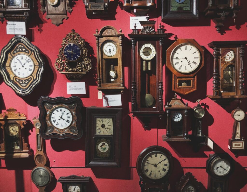 A diverse collection of vintage wall clocks displayed against a red wall in an antique shop.